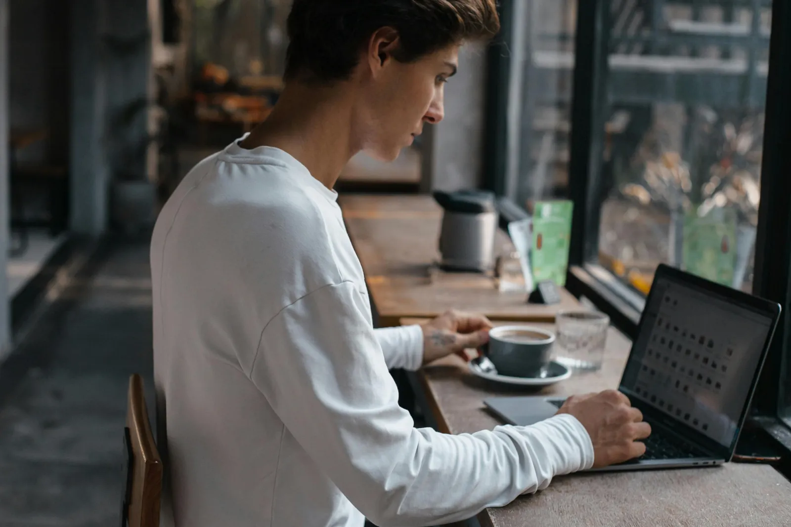 Mann fordypet i en laptop med en kopp kaffe på en kafé