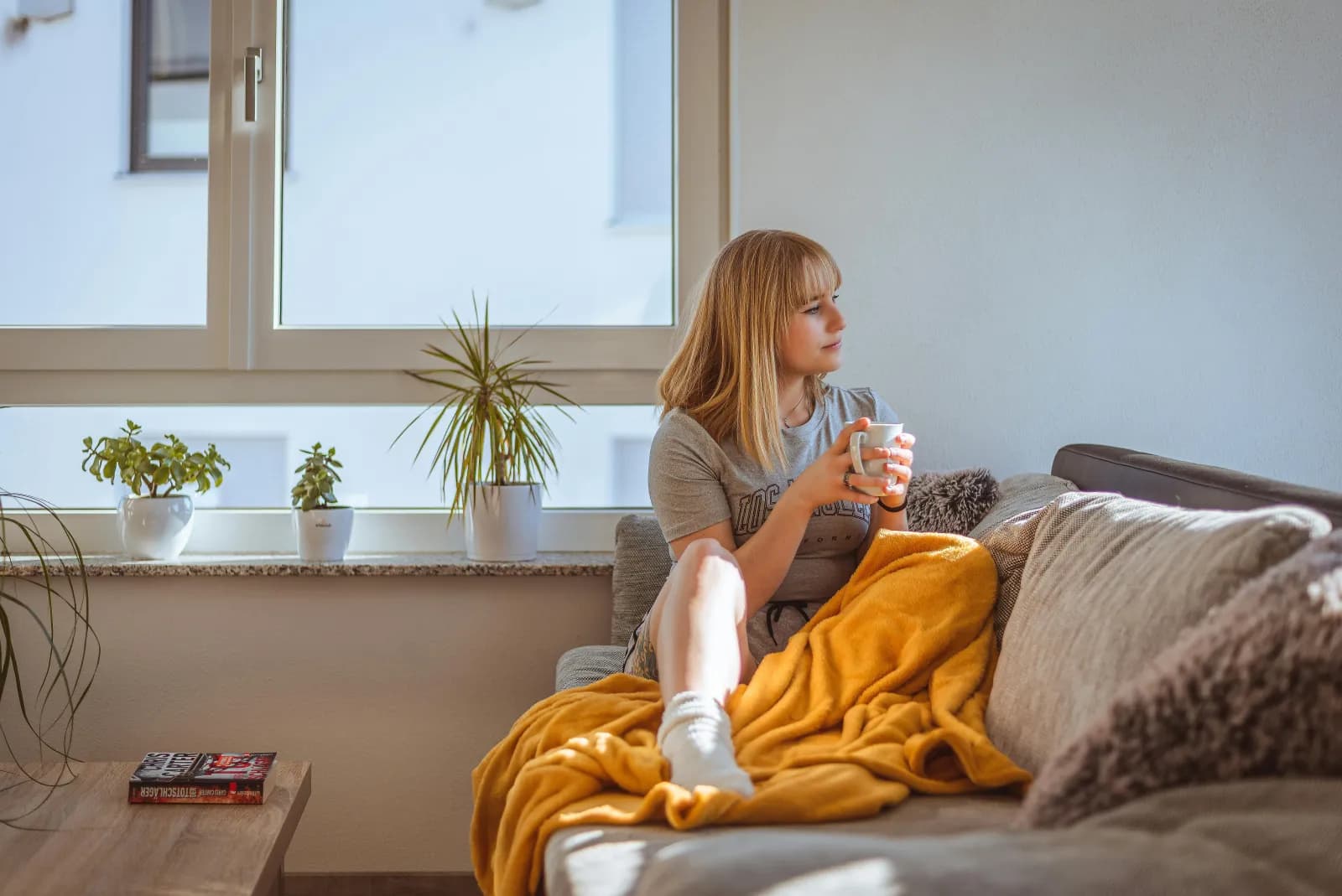 Kvinne med en kopp kaffe i sofaen ved vinduet